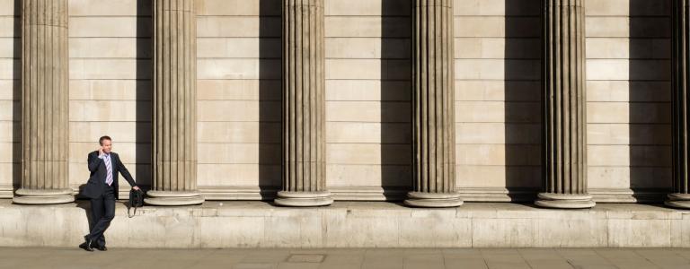 A man in a suit talks on a cell phone outside a bank in London with large columns