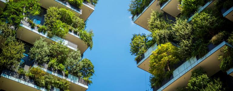 Two tall buildings with lots of greenery on their exteriors stand side-by-side with blue sky in between