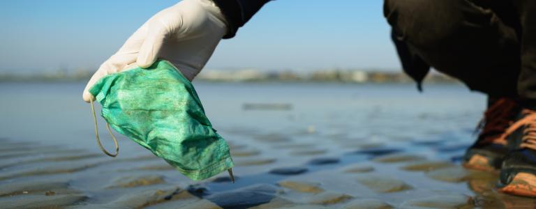 A person wearing a latex glove pulls a used face mask out of a lake