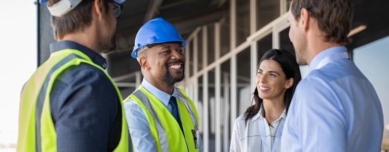 A Black man in construction hat and vest shakes hands with a man in a dress suit while smiling