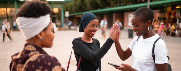 Three young women stand together at an outdoor market, with two high-fiving each other