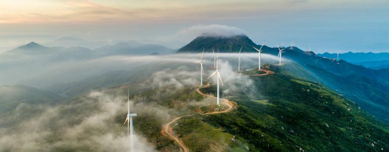 Wind turbines along a mountain ridge at sunset.