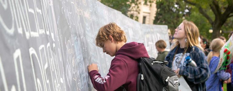 Young people in Winnipeg writing on a chalkboard outside during a climate strike