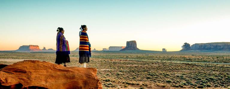 Navajo girls wrapped in handwoven traditional blankets enjoying a grand sunrise or sunset in Monument Valley