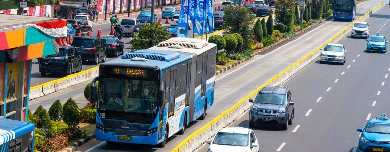 Buses in front of a colourful building beside a busy road.