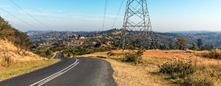 Power lines string alonside a road heading down rolling hills.