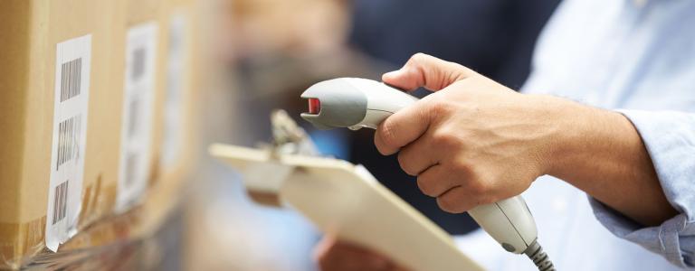 A worker scans a barcode on a box while holding a clipboard.