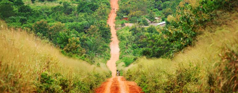 People can be seen in the distance travelling along a dirt road in rural Africa.