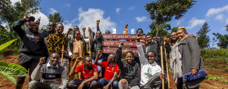 A group of young people stand in front of a sign in an African country