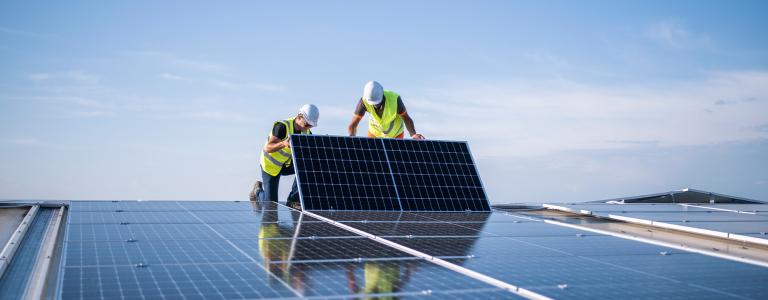 Two engineers install a solar panel on a roof.