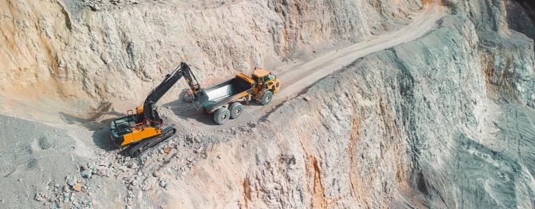 An excavator loads a dump truck with materials in a quarry.
