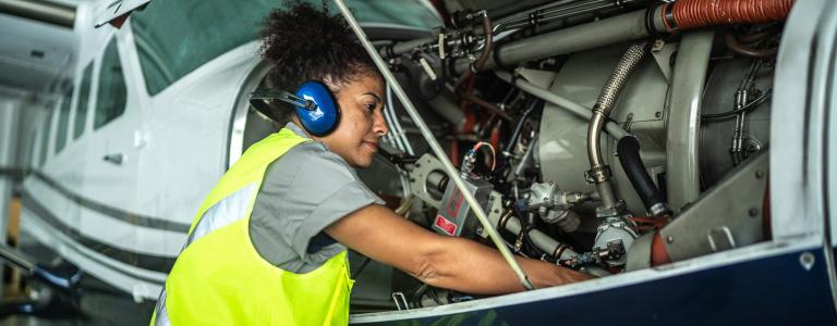 An aircraft mechanic repairs a plane in an airport hangar.