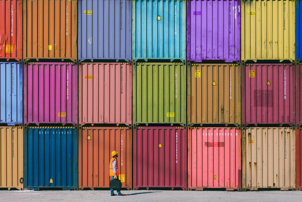 A man in construction vest walks by rows of colourful shipping containers