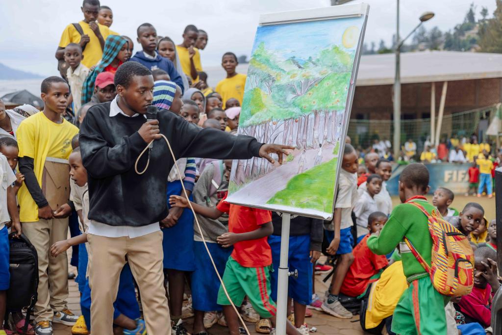 A student holds a microphone and points to an artwork, explaining its message to his peers.